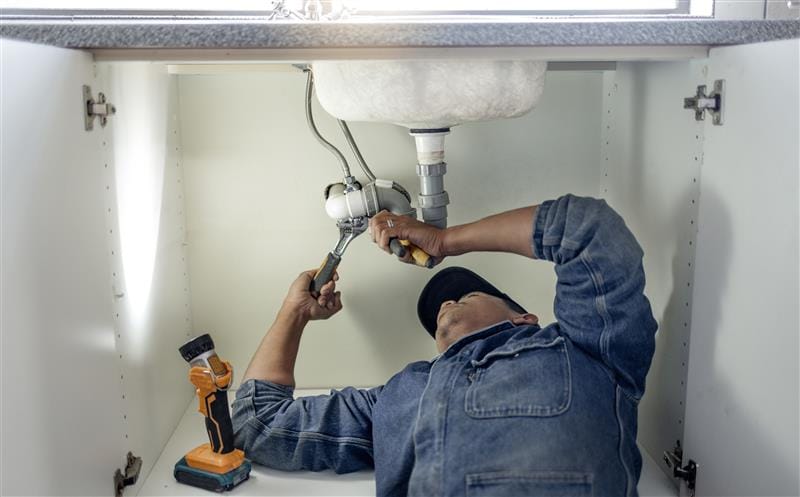 Plumber repairing pipes beneath a bathroom sink in Deerfield Beach