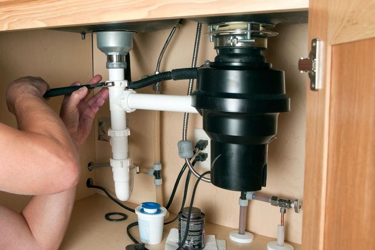 Plumber installing a garbage disposal beneath a kitchen sink in Deerfield Beach