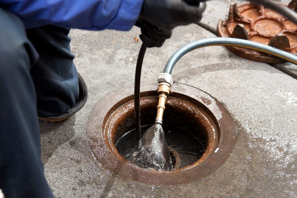 Plumber hydro jetting a sewer line through a manhole in Deerfield Beach