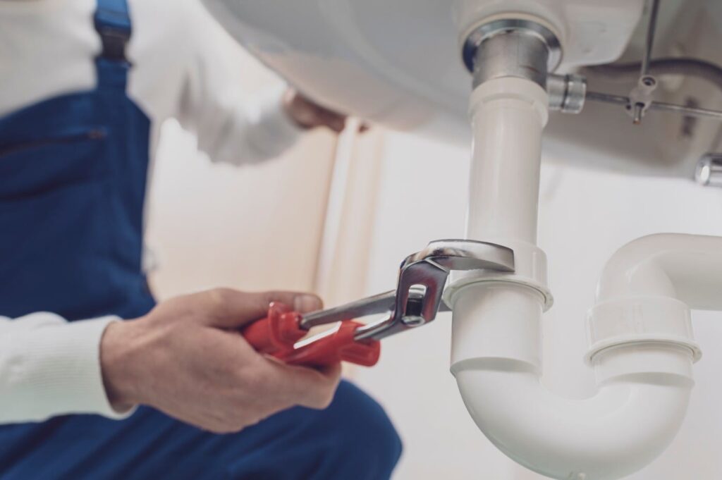 Plumber repairing a white drain pipe beneath a sink in Deerfield Beach