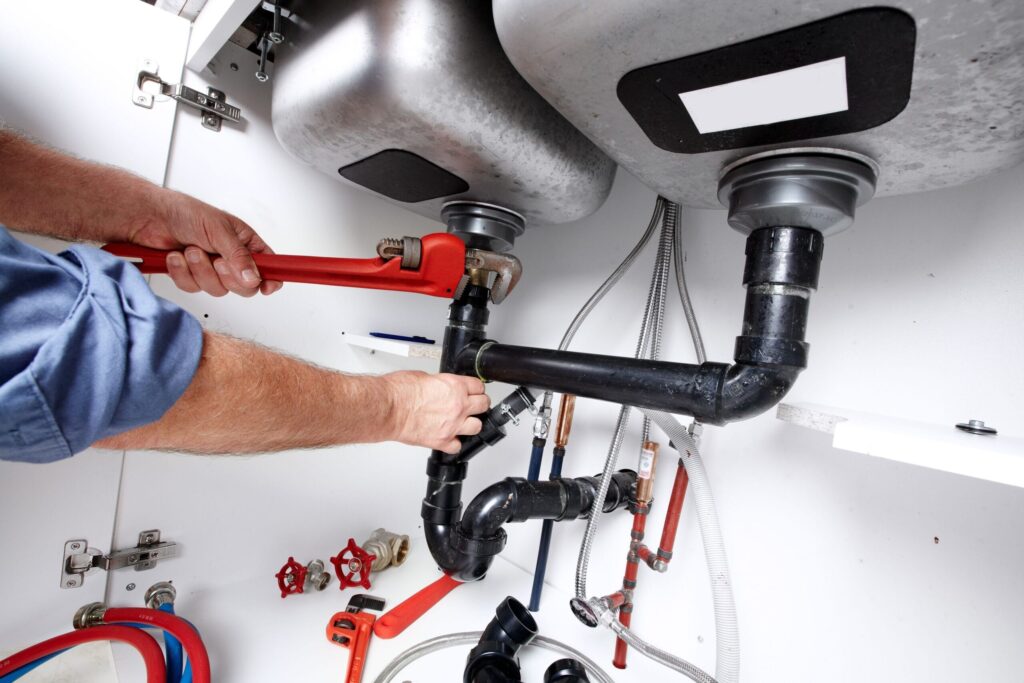 Plumber repairing drain pipes beneath a kitchen sink in Deerfield Beach