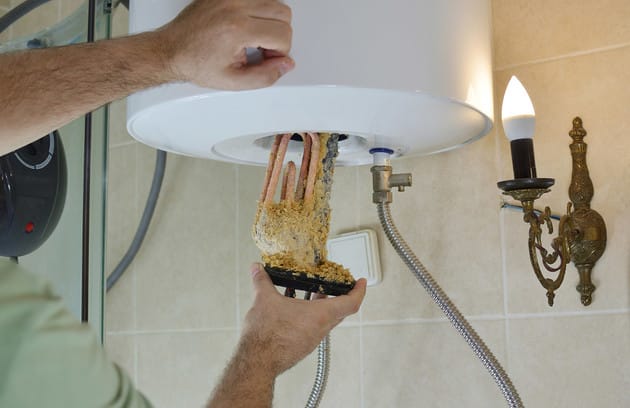 Technician removing mineral buildup from a water heater in Deerfield Beach